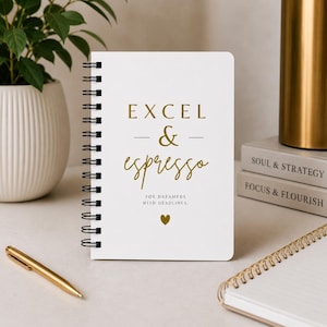 Może przedstawiać: Biały notatnik ze spiralą ze złotym napisem EXCEL & espresso FOR DREAMERS WITH DEADLINES oraz małą złotą ikoną serca. Notatnik znajduje się na powierzchni wraz ze złotym długopisem i drugim notatnikiem w pobliżu.