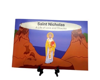 Könnte beinhalten: Ein Buch mit dem Titel "Saint Nicholas, A Life of Love and Miracles" wird auf einem schwarzen Ständer präsentiert. Das Cover zeigt eine Illustration von Saint Nicholas in gelben Gewändern, der ein rotes Buch hält, mit einem Landschaftshintergrund.
