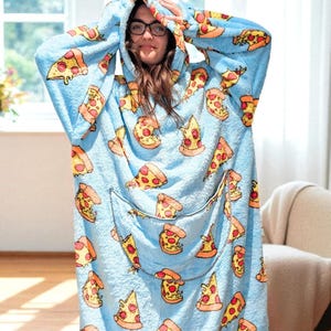 May include: A light blue hooded blanket with a pizza slice pattern. The blanket features a large front pocket and a hood. The pizza slices have yellow crusts, red sauce, and white cheese. The blanket is made of a soft, plush material.