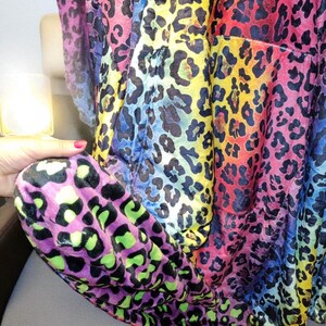 Puede incluir: Una tela estampada con estampado de leopardo multicolor. La tela presenta manchas negras y pasa por un arco&iacute;ris de colores, incluyendo rosa, amarillo, azul y morado. La tela est&aacute; drapeada sobre una superficie.