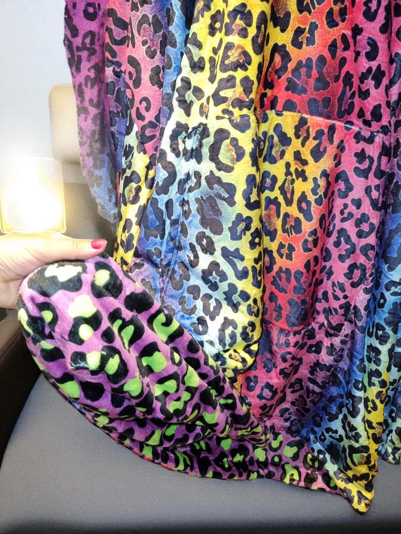 Puede incluir: Una tela estampada con estampado de leopardo multicolor. La tela presenta manchas negras y pasa por un arco&iacute;ris de colores, incluyendo rosa, amarillo, azul y morado. La tela est&aacute; drapeada sobre una superficie.