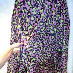 Puede incluir: Una manta con capucha con estampado de leopardo. La manta tiene una base morada con manchas negras y verde ne&oacute;n. Cuenta con una capucha y un gran bolsillo delantero. El material suave y afelpado est&aacute; dise&ntilde;ado para la comodidad y el calor.