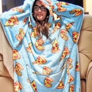 May include: A light blue hooded blanket with a pizza slice pattern. The blanket has a large front pocket and a hood. The pizza slices are yellow, red, and orange. The person wearing the blanket is smiling and wearing glasses.