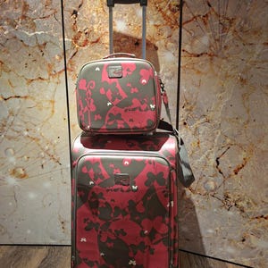 May include: A two-piece luggage set consisting of a large upright rolling suitcase and a smaller matching travel bag. Both pieces feature a dark gray base color with a repeating pattern of pink butterflies and a small rectangular logo patch.