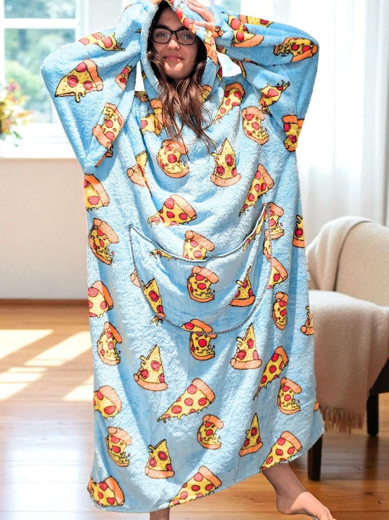 May include: A light blue hooded blanket with a pizza slice pattern. The blanket features a large front pocket and a hood. The pizza slices have yellow crusts, red sauce, and white cheese. The blanket is made of a soft, plush material.