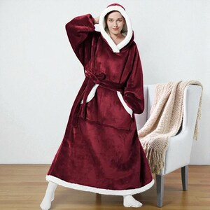 Puede incluir: Una manta con capucha burdeos con ribete blanco y cinturón a juego. La manta tiene un bolsillo delantero grande y está diseñada para ser usada. La modelo lleva calcetines blancos.