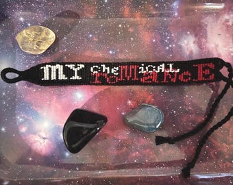 May include: Black friendship bracelet with the text "MY CHEMICAL ROMANCE" in white and red. The bracelet is accompanied by three polished stones: a clear, a black, and a blue-gray stone. The background is a galaxy design.