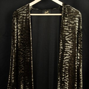 May include: A long, open-front cardigan with a brown and cream zebra print pattern. The garment is hanging on a wooden hanger against a black backdrop. The label reads "Arelle London".