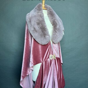May include: A dusty rose velvet cape with a faux fur collar. The cape features a decorative gold-colored clasp at the waist. The brand name "EdenJonesCo" is printed at the top of the image.