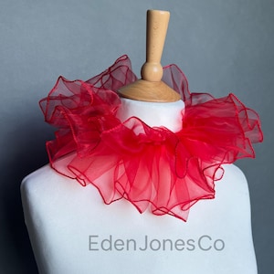 Könnte beinhalten: Ein leuchtend roter Rüschenkragen aus transparentem Stoff, präsentiert auf einer weißen Schaufensterpuppe. Der Kragen hat ein mehrschichtiges Design mit einem gewellten Rand. Der Text "Eden Jones Co" ist auf der Schaufensterpuppe zu sehen.