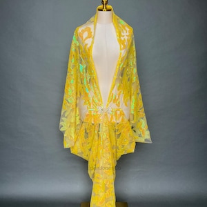 Puede incluir: Un chal amarillo con lentejuelas y motivos florales se exhibe en un maniquí. El chal tiene un diseño de cuello en V y una broche decorativa en la cintura. La marca "EdenJonesCo" es visible en la esquina superior izquierda e inferior derecha.