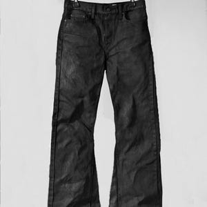 May include: Black denim jeans with a slight flare at the bottom, hanging from a black hanger. The jeans have a classic five-pocket design and a dark, textured appearance. The pants are displayed against a plain white background.