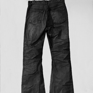 May include: Black denim jeans with a flared leg design, hanging from a black hanger. The jeans have two back pockets and a classic five-pocket style. The fabric appears to have a slight sheen.