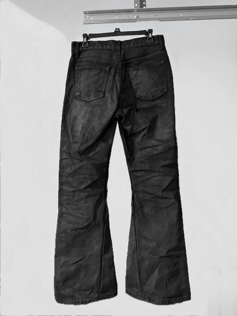 May include: Black denim jeans with a flared leg design, hanging from a black hanger. The jeans have two back pockets and a classic five-pocket style. The fabric appears to have a slight sheen.