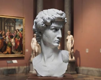 May include: A white marble bust of a young person with curly hair, depicted with a focused expression and turned head. The sculpture features detailed facial contours and is positioned on a dark brown wooden pedestal within a gallery space.