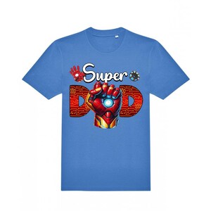 May include: A light blue t-shirt with a graphic design. The design features the words "Super Dad" with a red and gold Iron Man-style hand and the letter "D" in a circuit board pattern. The shirt is a crew neck.