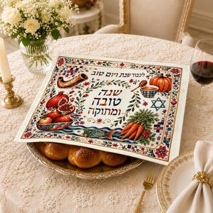 May include: A rectangular placemat featuring a colorful Rosh Hashanah illustration with Hebrew text, pomegranates, a shofar, a pumpkin, carrots, and a fish, covering a silver platter holding a braided challah bread loaf on a lace tablecloth.