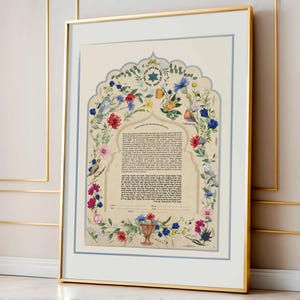 May include: Framed Ketubah art print with a floral arch design. The artwork features a cream-colored background with a blue border. The arch is adorned with colorful flowers, birds, and text. The frame is gold.