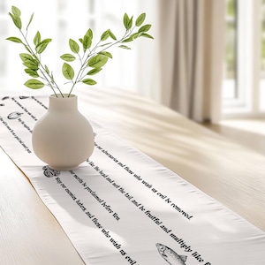 May include: A white table runner featuring black printed text and illustrations of a fish and a pumpkin. The text includes phrases such as May our enemies, haters, and those who wish us evil be removed and May our merits be proclaimed before You.