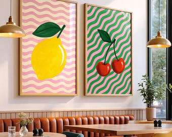 Könnte beinhalten: Zwei gerahmte Kunstwerke. Eines zeigt eine gelbe Zitrone mit einem grünen Blatt auf einem rosa-weißen Wellenhintergrund. Das andere zeigt zwei rote Kirschen mit einem grünen Stiel auf einem grün-rosa Wellenhintergrund. Beide sind in Holzrahmen.