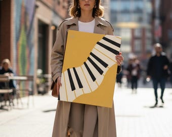 May include: A mustard yellow canvas art piece featuring a stylized piano keyboard design with black and white keys. The artwork is held by a person in a tan trench coat, suggesting a fashion or home decor theme.