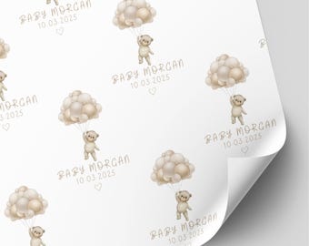May include: White wrapping paper featuring a repeating pattern of watercolor-style light brown teddy bears holding clusters of beige and cream-colored balloons. The text BABY MORGAN 10.03.2025 and a small heart icon are printed below each bear.