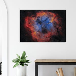 Op de afbeelding: Een levendige canvas print die een nevel in de ruimte afbeeldt. Het kunstwerk toont een mix van kleuren, waaronder diep rood, oranje en blauw, tegen een donkere achtergrond. De hemelse scène is een boeiend kunstwerk.
