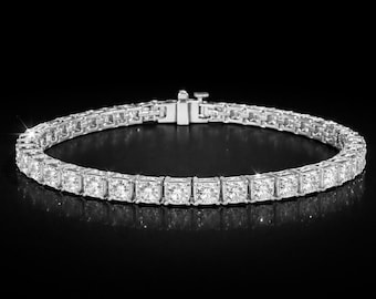 May include: A silver-toned tennis bracelet featuring a continuous row of square-cut, clear, faceted stones set in a metallic frame. The bracelet includes a secure box clasp mechanism at the top, showcasing a polished finish and reflective surfaces.