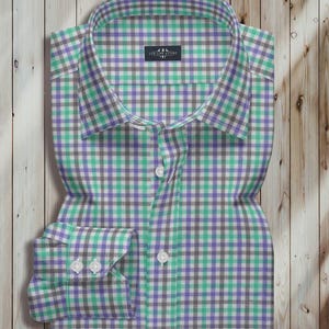 May include: A folded dress shirt with a checkered pattern in shades of green, purple, gray, and white. The shirt has a classic collar and buttoned cuffs. The label reads "LUX LINE ATTIRE".