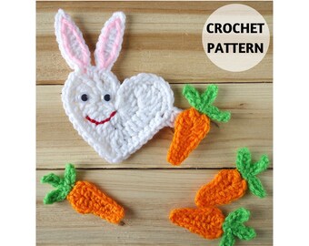May include: A white heart-shaped crochet bunny with pink-lined ears, googly eyes, and a red stitched mouth, accompanied by three small orange crochet carrots with green tops. The image includes the text CROCHET PATTERN and GoldenLucyCrafts.