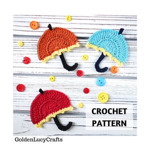 May include: Three crocheted umbrellas in red, orange, and blue with yellow trim. The umbrellas are on a white wooden background with colorful buttons scattered around them. The text "CROCHET PATTERN" is written in black letters on the bottom right of the image.
