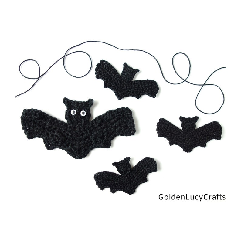 May include: Four black crocheted bats with white eyes. The bats are of different sizes and are arranged on a white background. There is a black string in the background.