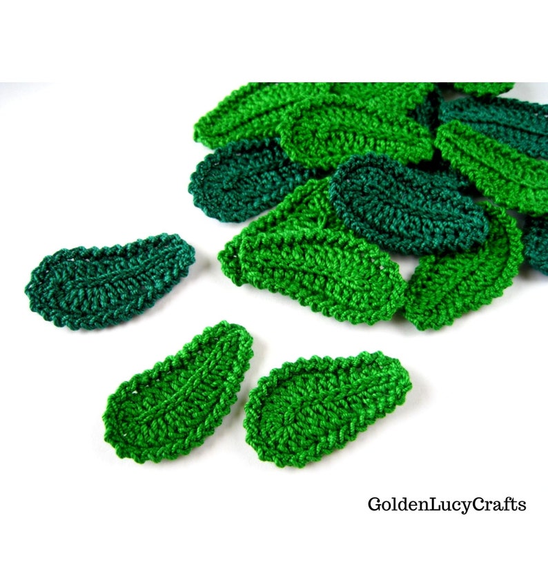 May include: A collection of green crocheted leaf shapes. The leaves are made with a textured stitch and have a slightly oval shape.