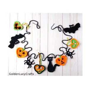 May include: A Halloween garland with black bats, spiders, cats, and pumpkins in orange, green, and black. The garland is made of crocheted felt and is strung together with black yarn. The garland is hanging on a white wooden background. The text "GoldenLucyCrafts" is visible in the bottom left corner of the image.