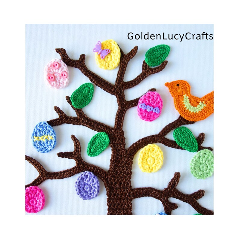 Puede incluir: Un &aacute;rbol de crochet marr&oacute;n decorado con huevos, hojas y un p&aacute;jaro de crochet de colores vivos. El &aacute;rbol est&aacute; adornado con botones y una mariposa. El texto "GoldenLucyCrafts" es visible en la parte superior de la imagen.