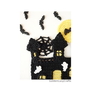 May include: Black crocheted haunted house with a yellow moon and bats. The house has a spider web on top and white ghost appliques.