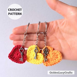 May include: Three crochet heart keychains in red, yellow, and orange, each with a silver key charm. The keychains are attached to silver key rings. The image includes the text "CROCHET PATTERN" and "GoldenLucyCrafts".