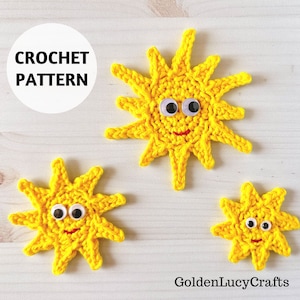May include: Three crocheted yellow suns with googly eyes and a red smile. The suns are different sizes and are arranged on a white wooden background. The text "CROCHET PATTERN" is written in a white circle on the top left of the image.