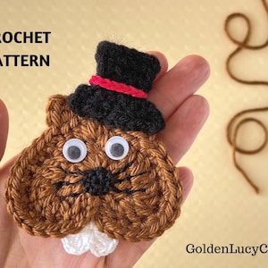 May include: Crochet pattern for a brown crocheted groundhog wearing a black top hat with a red band and white googly eyes. The text "CROCHET PATTERN" is at the top of the image.