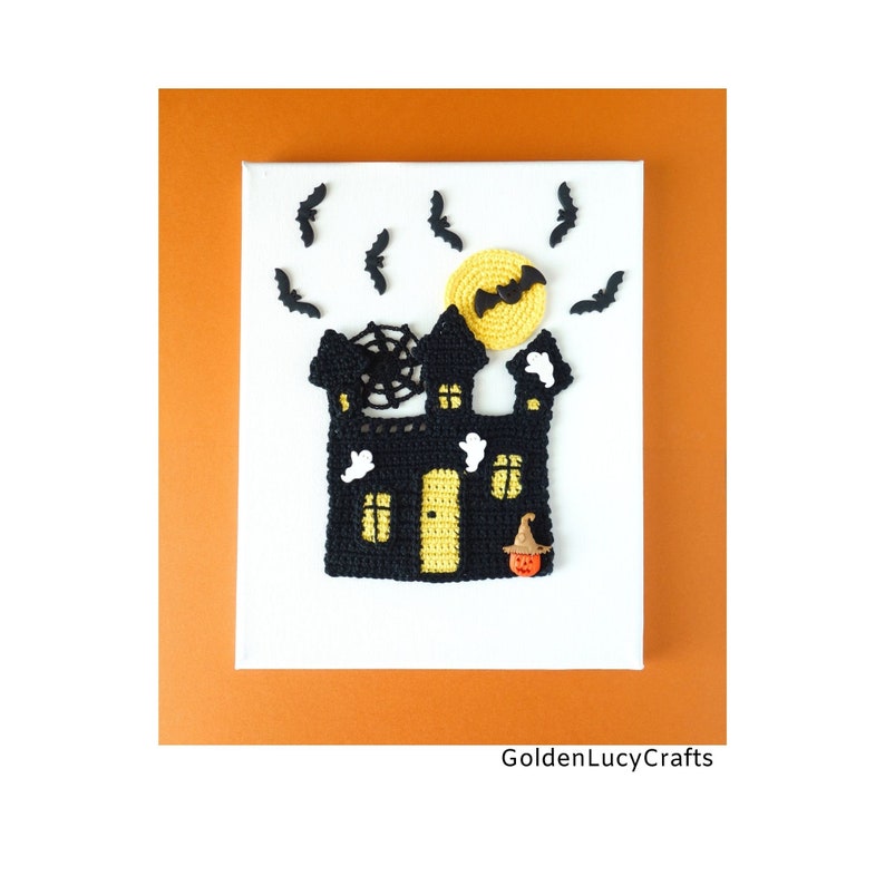 May include: A crocheted Halloween-themed wall art piece featuring a black haunted house with a yellow door and windows, a spider web, and a witch's hat. The house is surrounded by black bats and a yellow moon. The art is displayed on a white canvas with the text "GoldenLucyCrafts" at the bottom.