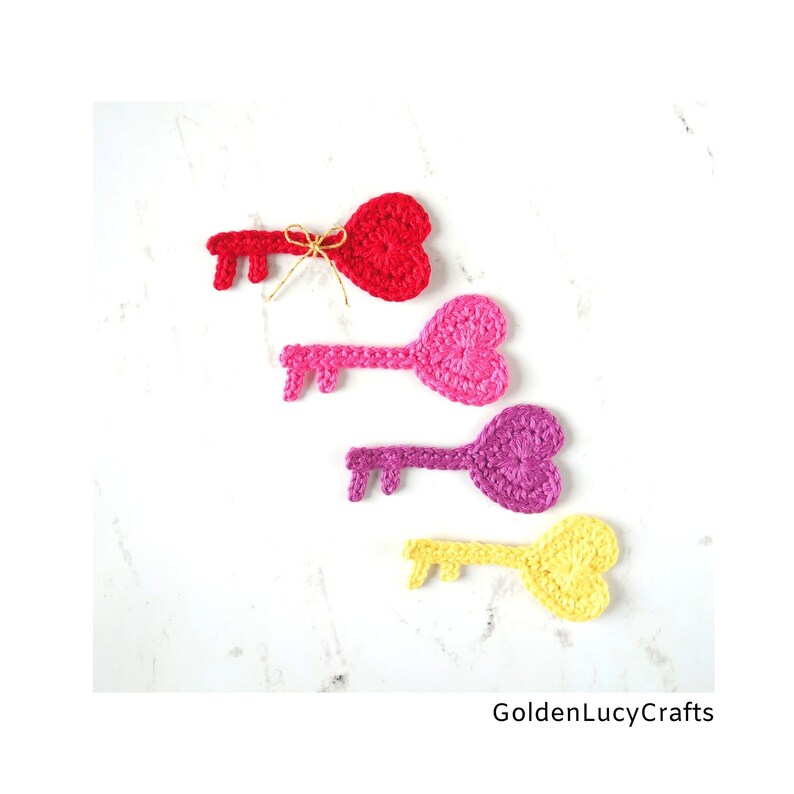 May include: Four crocheted heart-shaped keys in red, pink, purple, and yellow. The keys are arranged vertically, with the red key at the top and the yellow key at the bottom. The keys are all tied with a gold ribbon.