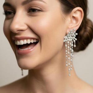 May include: Elegant diamond earrings with a cascading design. The earrings feature a cluster of sparkling stones at the top, with multiple strands of smaller diamonds hanging below. The earrings are a bright, clear white, and reflect light beautifully.