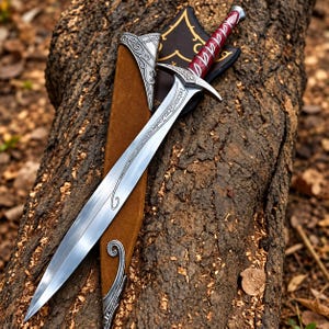 May include: A silver-toned sword with a pointed blade featuring etched script, a curved crossguard, and a deep red handle with silver accents. The sword rests on a brown suede scabbard with ornate silver metal fittings at the tip and throat.