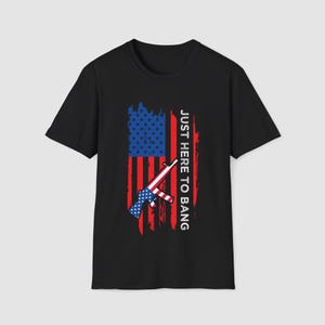 May include: Black t-shirt with a graphic of the American flag and a rifle, alongside the text "JUST HERE TO BANG" in white. The flag design is red, white, and blue.