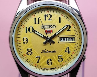 Reloj Seiko 5 automático reacondicionado, esfera amarilla, correa de cuero marrón, día y fecha, acero inoxidable, vintage.