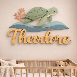 Peut inclure: Une enseigne murale en bois représentant une tortue de mer vert clair nageant au-dessus de vagues bleues superposées et d'une branche de corail pêche. Le prénom Theodore est écrit en grandes lettres cursives en bois brun clair.