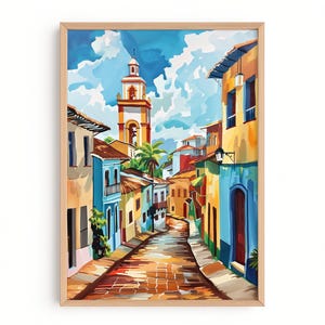 Peut inclure: Une peinture encadrée à l'aquarelle d'une scène de rue colorée. L'œuvre représente une rue pavée étroite bordée de bâtiments bleus, jaunes et oranges. Un grand clocher se dresse au loin sous un ciel bleu vif avec des nuages blancs duveteux.