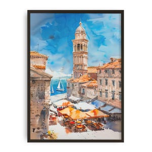 Może przedstawiać: Akwarela europejskiego krajobrazu miejskiego z wysoką dzwonnicą i budynkami z pomarańczowymi dachami. Scena obejmuje miejsca do siedzenia na zewnątrz z pomarańczowymi parasolami, żaglówki na wodzie i jasnoniebieskie niebo. Grafika jest oprawiona w czarną ramę.