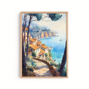 May include: Watercolour painting of a coastal village with orange-tiled roofs and a stone pathway. The artwork depicts a serene seascape with a sailboat on the blue water. The painting is framed in a light wood frame.