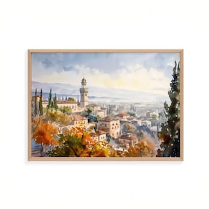 May include: Watercolor painting of a European townscape in a wooden frame. The artwork depicts buildings with red tile roofs, a tall tower, and lush trees in shades of green and orange. The sky is a soft blue with hints of yellow.